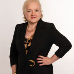 Yana-Anders-Personal-Stylist-at-Style-Fix-Studio - Style Fix Studio Professional portrait of a confident woman with short blonde hair, wearing a black blazer and gold jewelry.