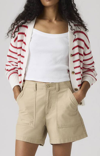 6A-Summer-Shorts - Style Fix Studio Woman wearing a white tank top with a cream-red striped cardigan and beige shorts with front pockets, posing with hands in pockets.