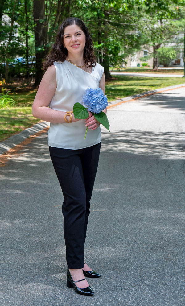 Woman standing on a tree-lined street, holding a blue hydrangea bouquet and smiling.