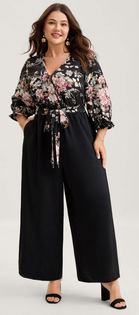 Apple-Black - Style Fix Studio Plus-size model wearing a black floral wrap top with a tied waist and wide-leg black pants, accessorized with gold earrings.