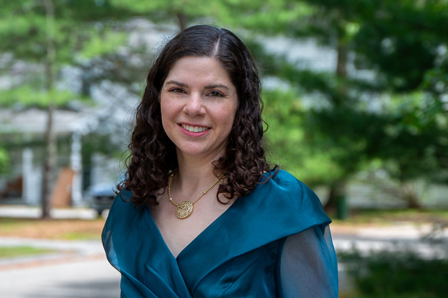 Summer-in-Silk-Elissa99-900 - Style Fix Studio Woman with curly dark hair smiling outdoors, wearing a teal dress and a gold pendant necklace.